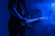 Guitar advertising banner. Male guitarist plays music in neon light with smoke.