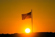 American flag on flagpole is back lit by setting sun.